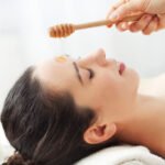 Woman waits patiently as a hand pours honey onto her face for a face mask
